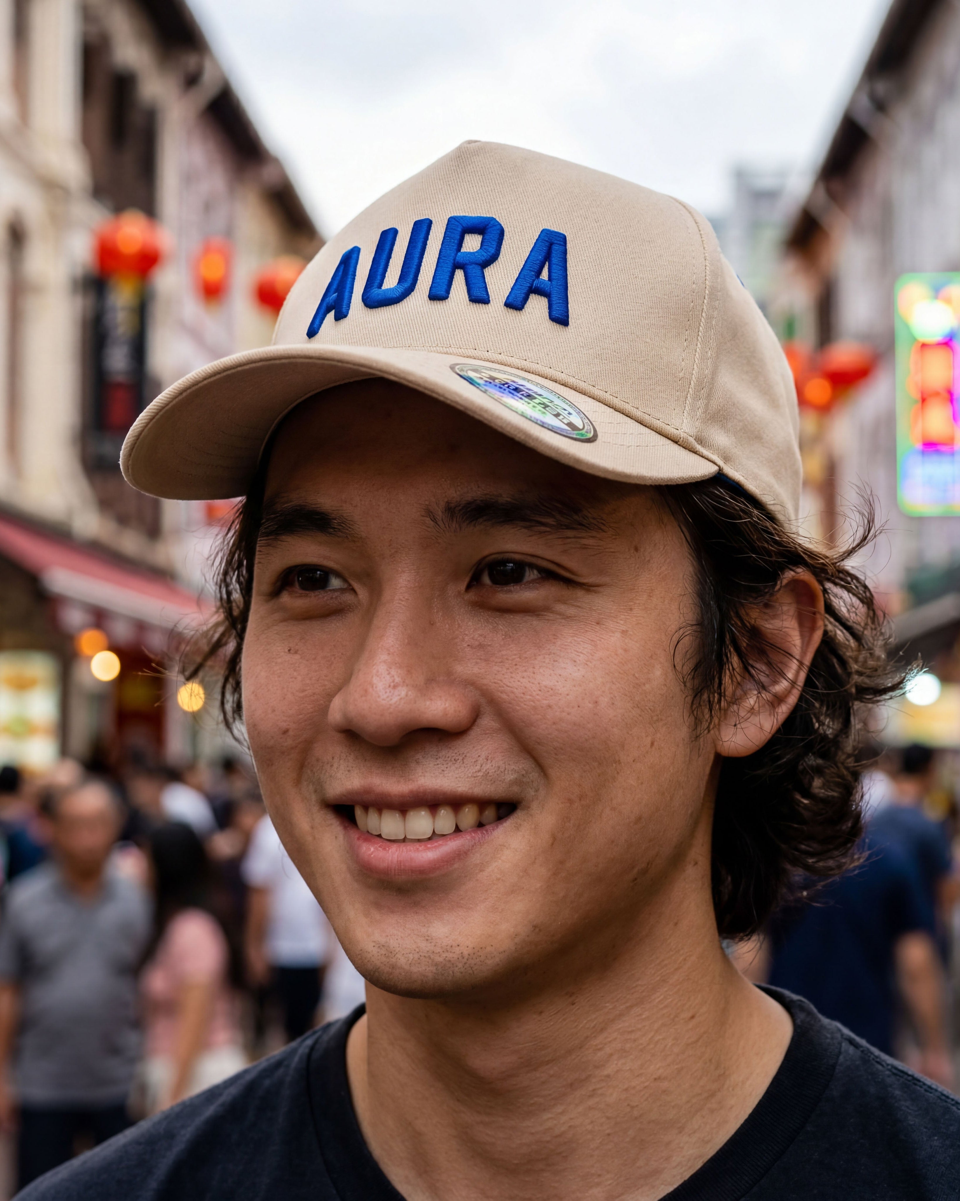 Man wearing a beige cap with 'AURA' on it in a busy street.