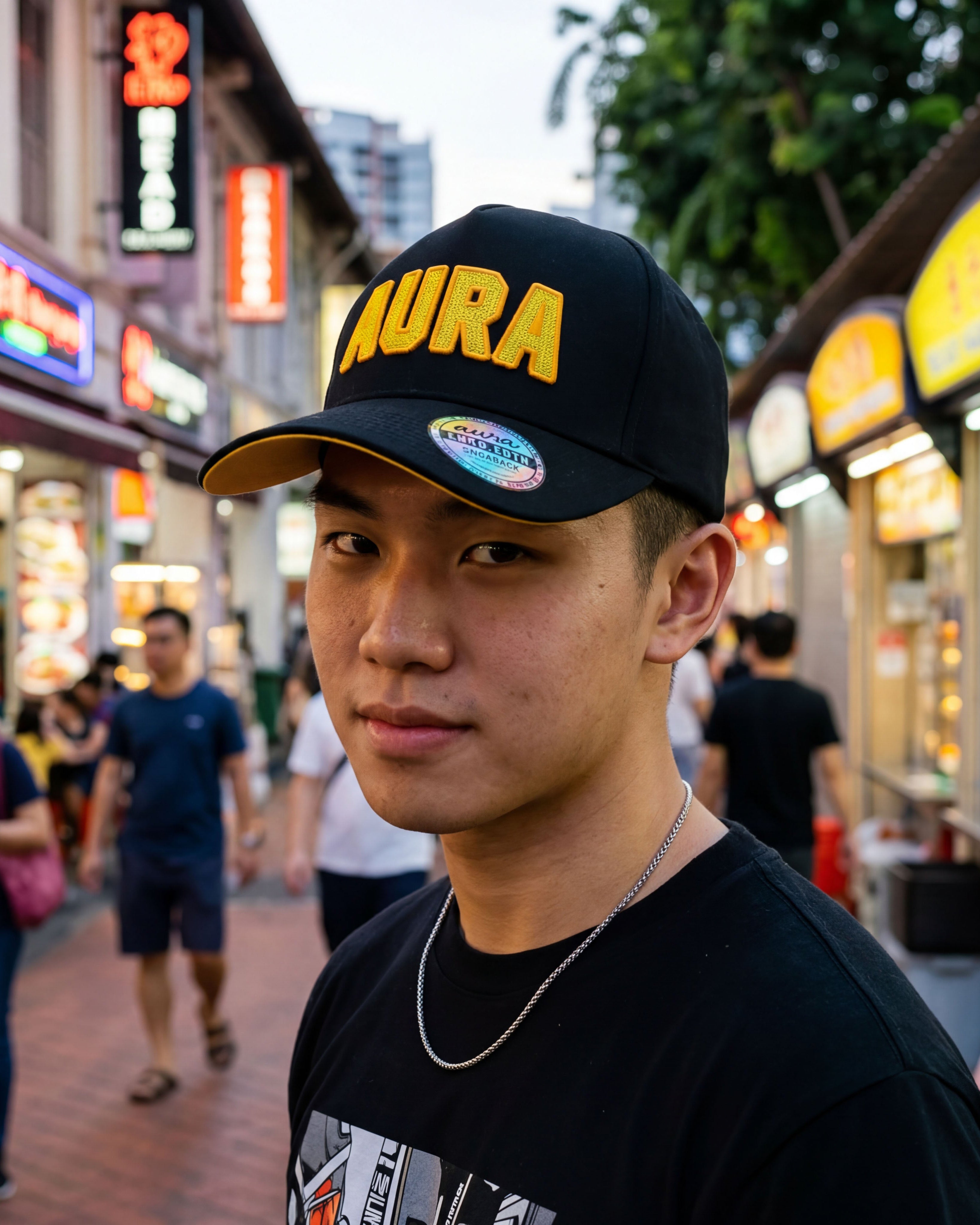 Person wearing a black cap with 'AURA' in yellow on a busy street with neon signs.