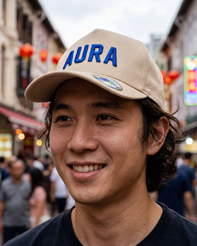 Man wearing a beige cap with 'AURA' on it in a busy street.